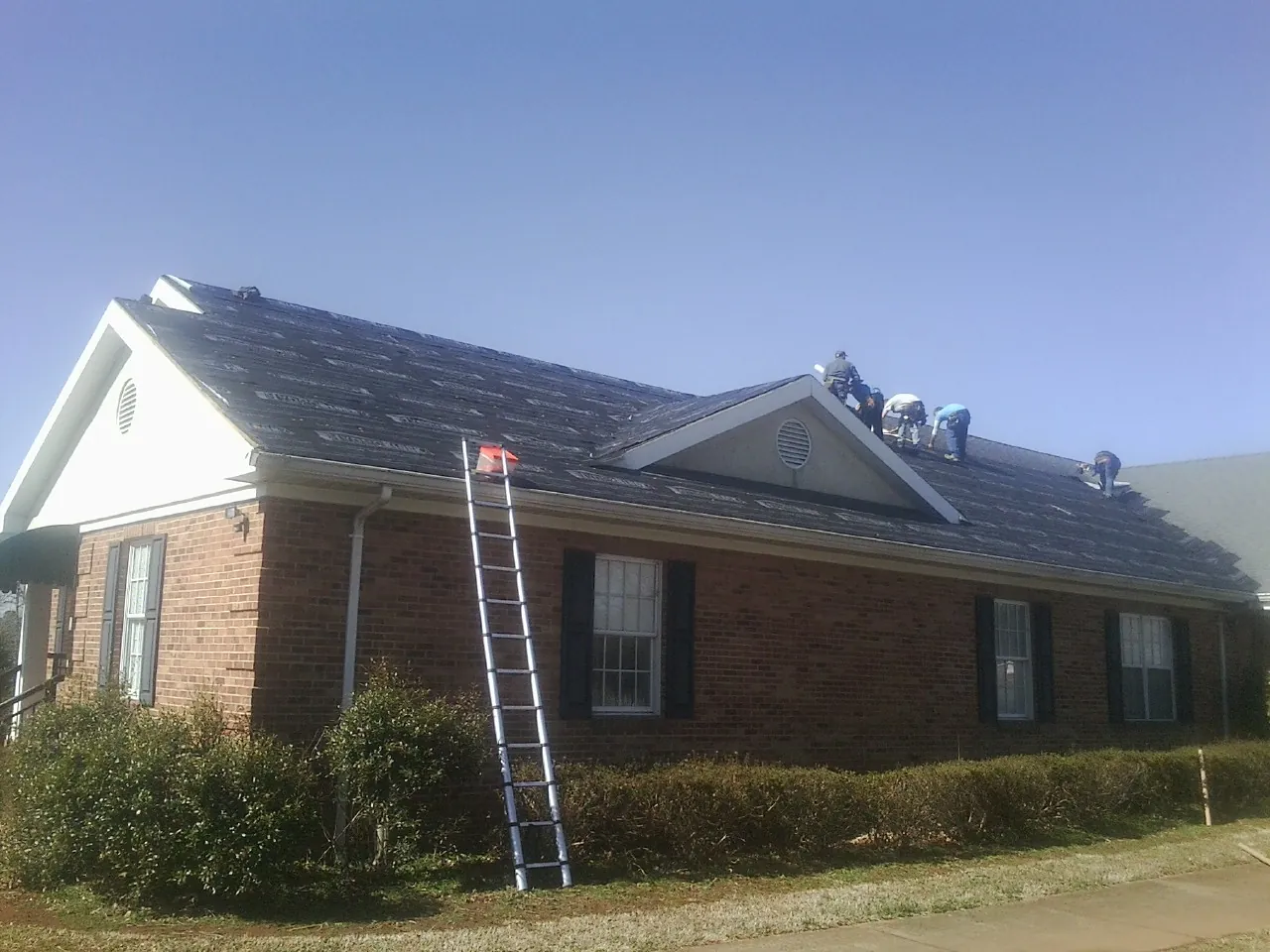 Crew tearing shingles off a brick ranch roof with a ladder set — Metal Roof Repair work by our crew in Petersburg