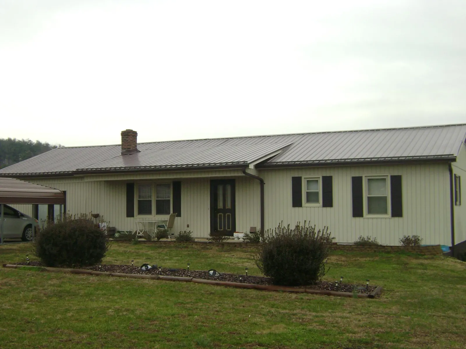 Brown metal roof on a cream sided ranch home with a brick chimney in Petersburg