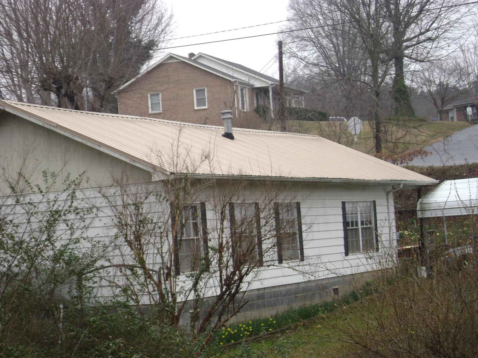 Tan metal roof on a white sided house set into a hillside — Commercial Roofing by Roofing Brothers in Petersburg